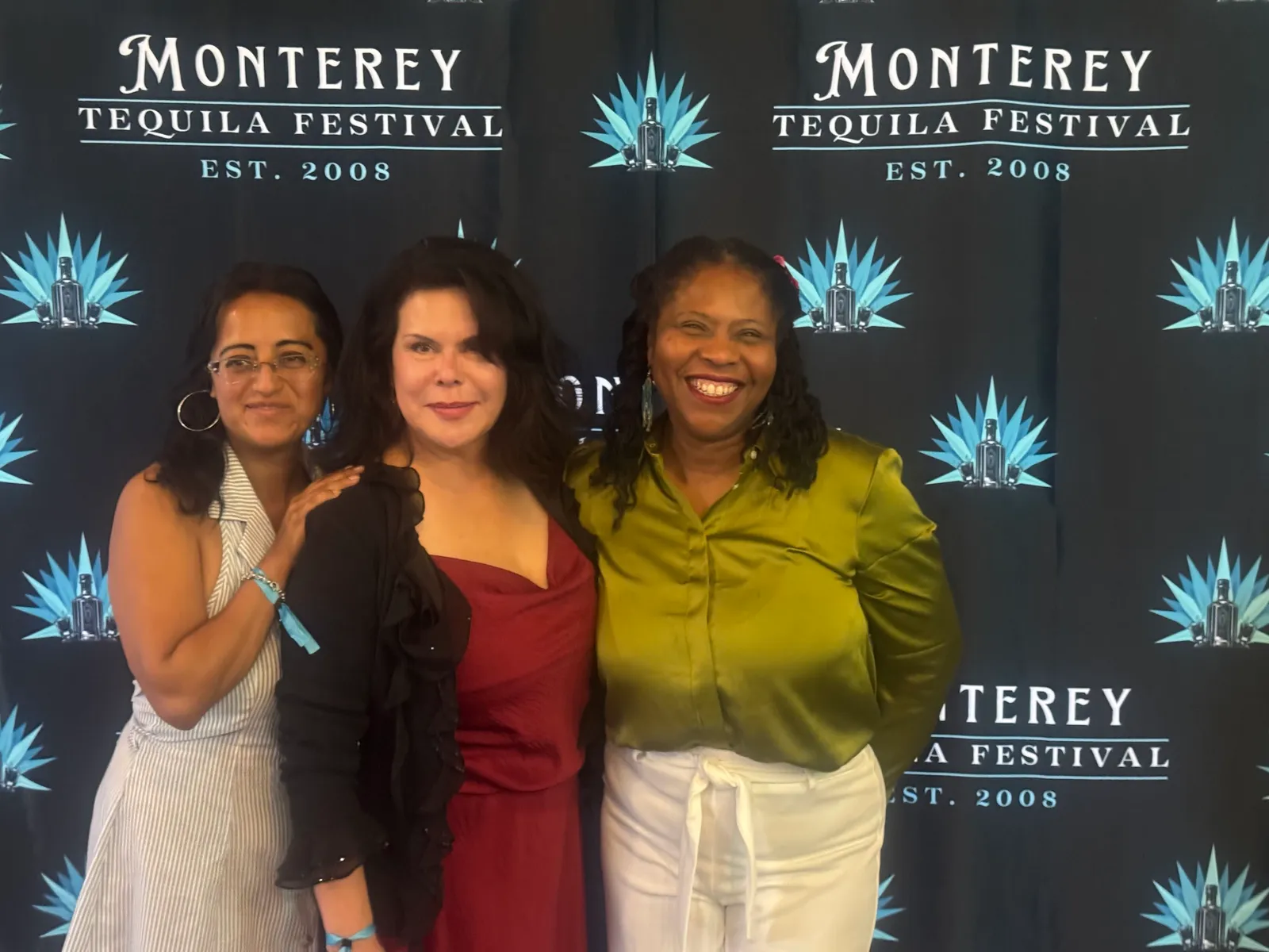 Three women smiling in front of the Monterey Tequila Festival backdrop