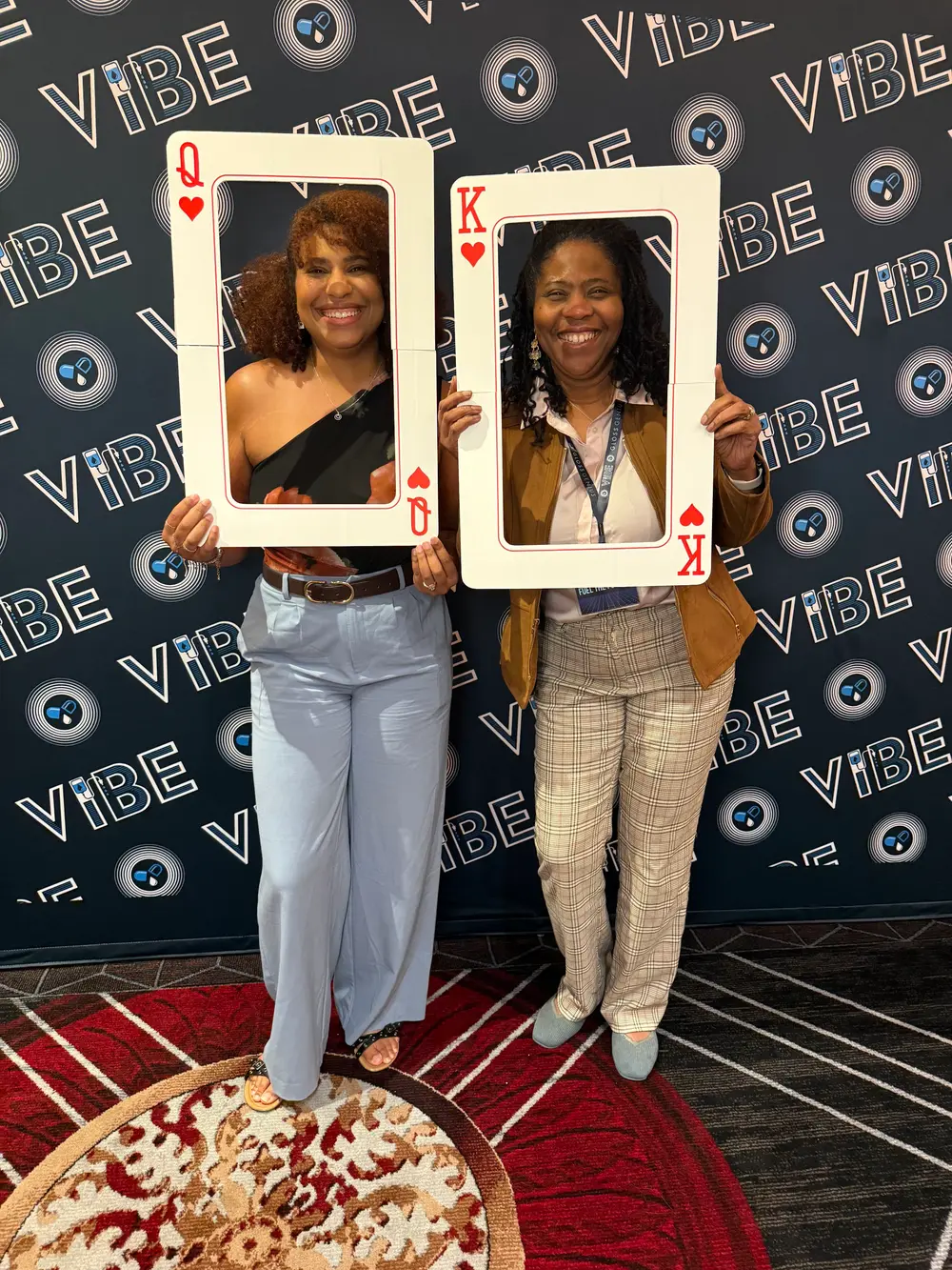 Two women posing with giant playing card frames at the VIBE Conference photo wall